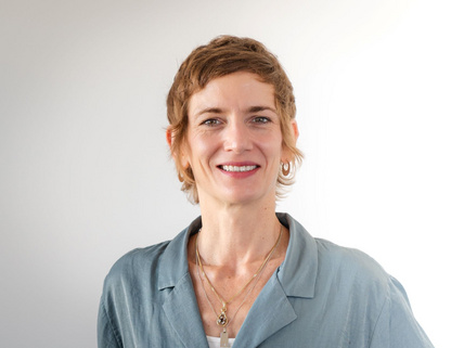 Portraitaufnahme von Sophia Wirsching. Sie steht vor einer wei&szlig;-grauen Wand und tr&auml;gt eine hellblau-gr&auml;uliche Bluse. Sophia Wirsching hat kurze dunkelblonde Haare und tr&auml;gt Ketten sowie Ohrringe und l&auml;chelt in die Kamera.